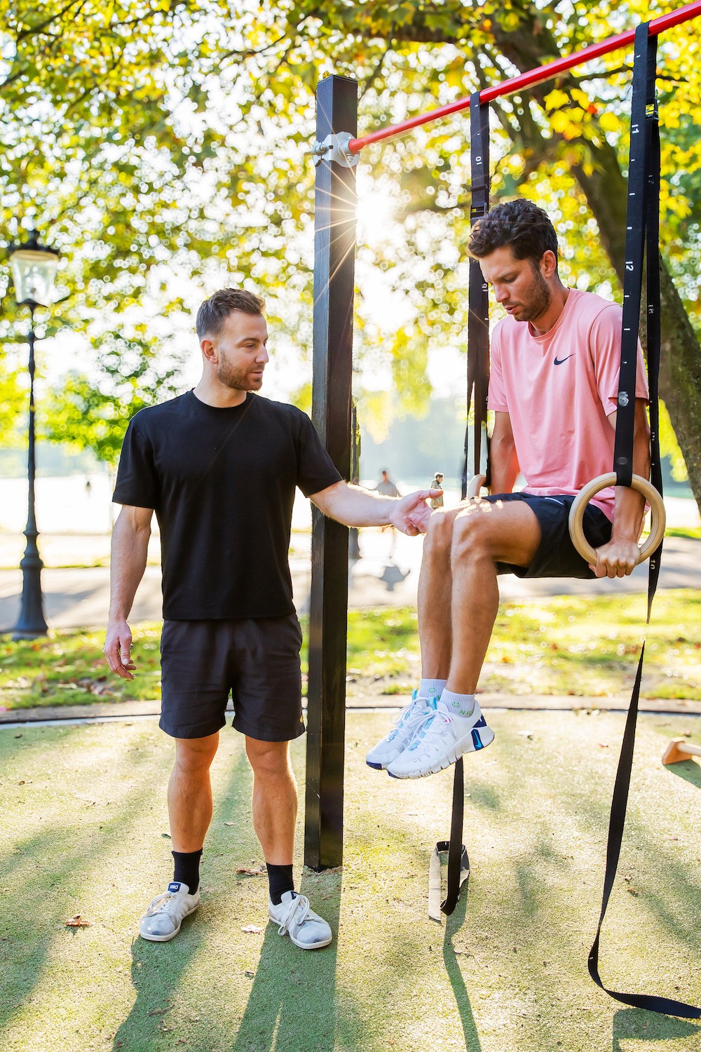 Rik Buijze coaching a client through a ring exercise at an outdoor calisthenics park